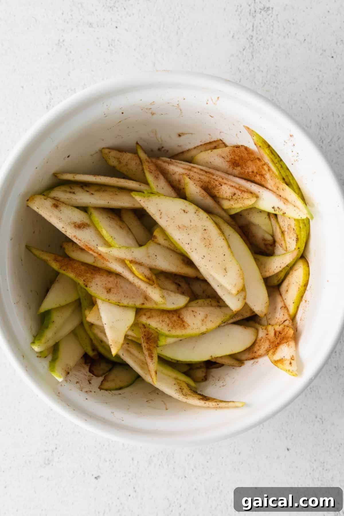 Thinly sliced pears tossed with spices in a large bowl, ready for assembly.