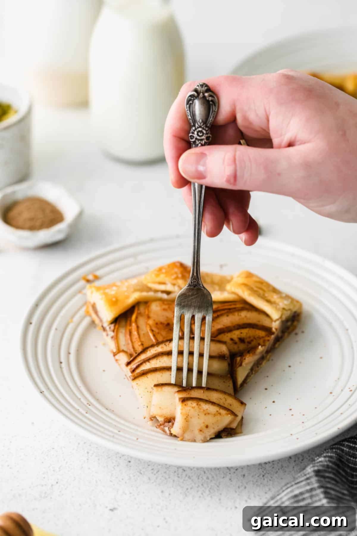 A hand holding a piece of honey pear galette, showing the delicious filling and crust.