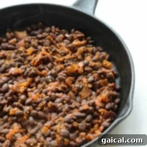 Sautéed black beans simmering in a cast iron skillet, seasoned with herbs and spices for a flavorful base.