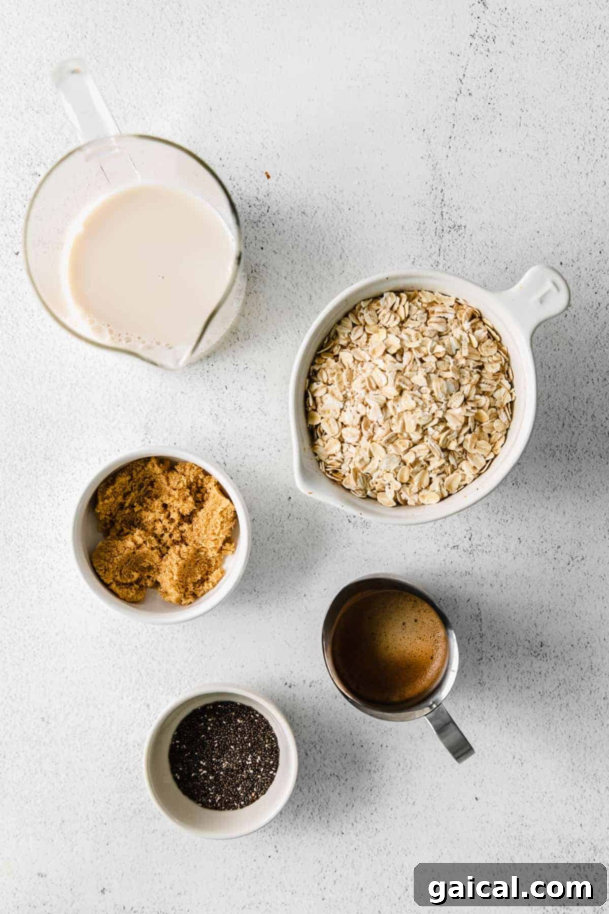 Ingredients for overnight oats laid out on a kitchen counter: rolled oats, brown sugar, chia seeds, almond milk, and espresso concentrate.