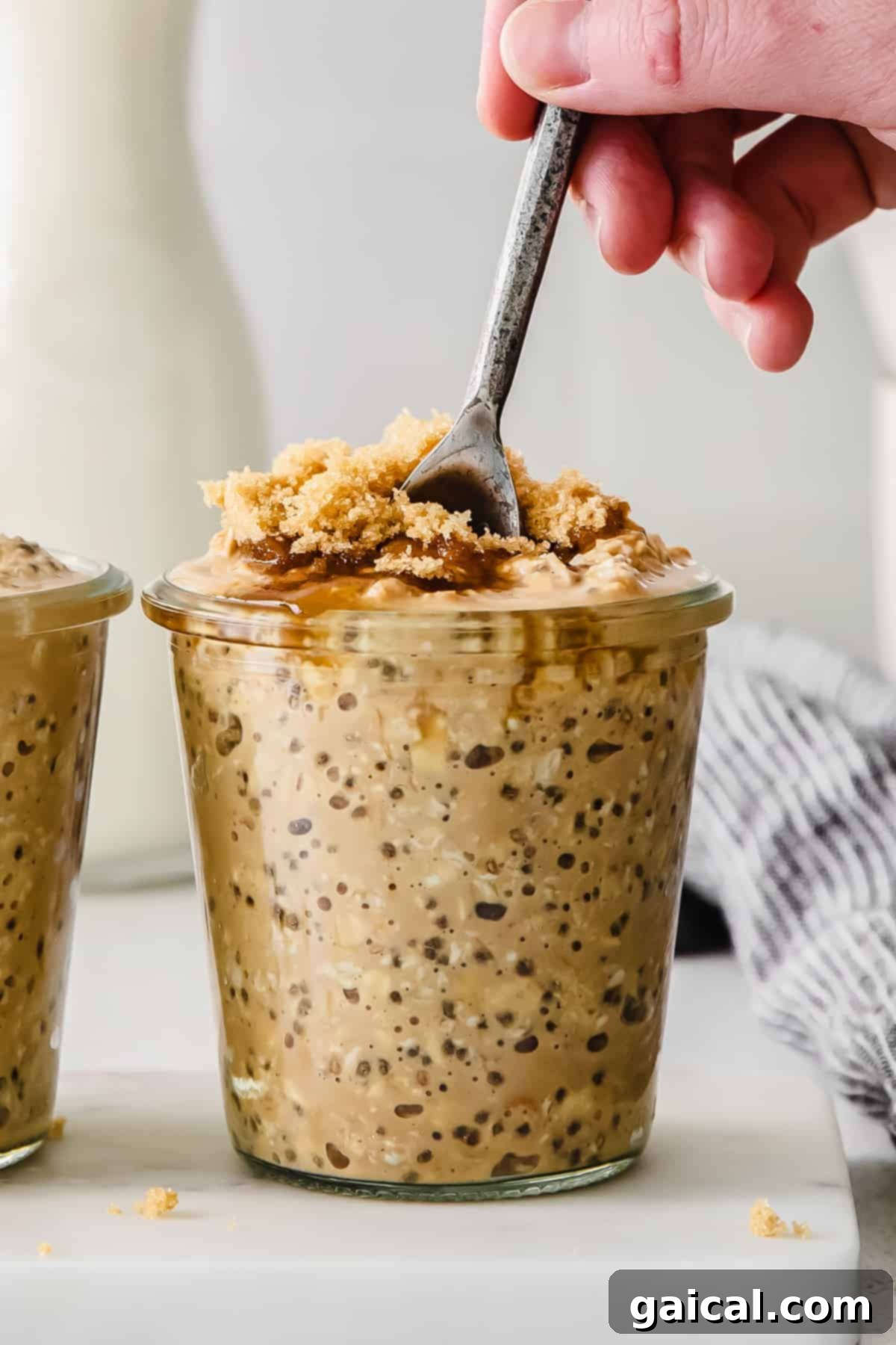 A jar of brown sugar shaken espresso overnight oats, topped with extra brown sugar and a spoon.