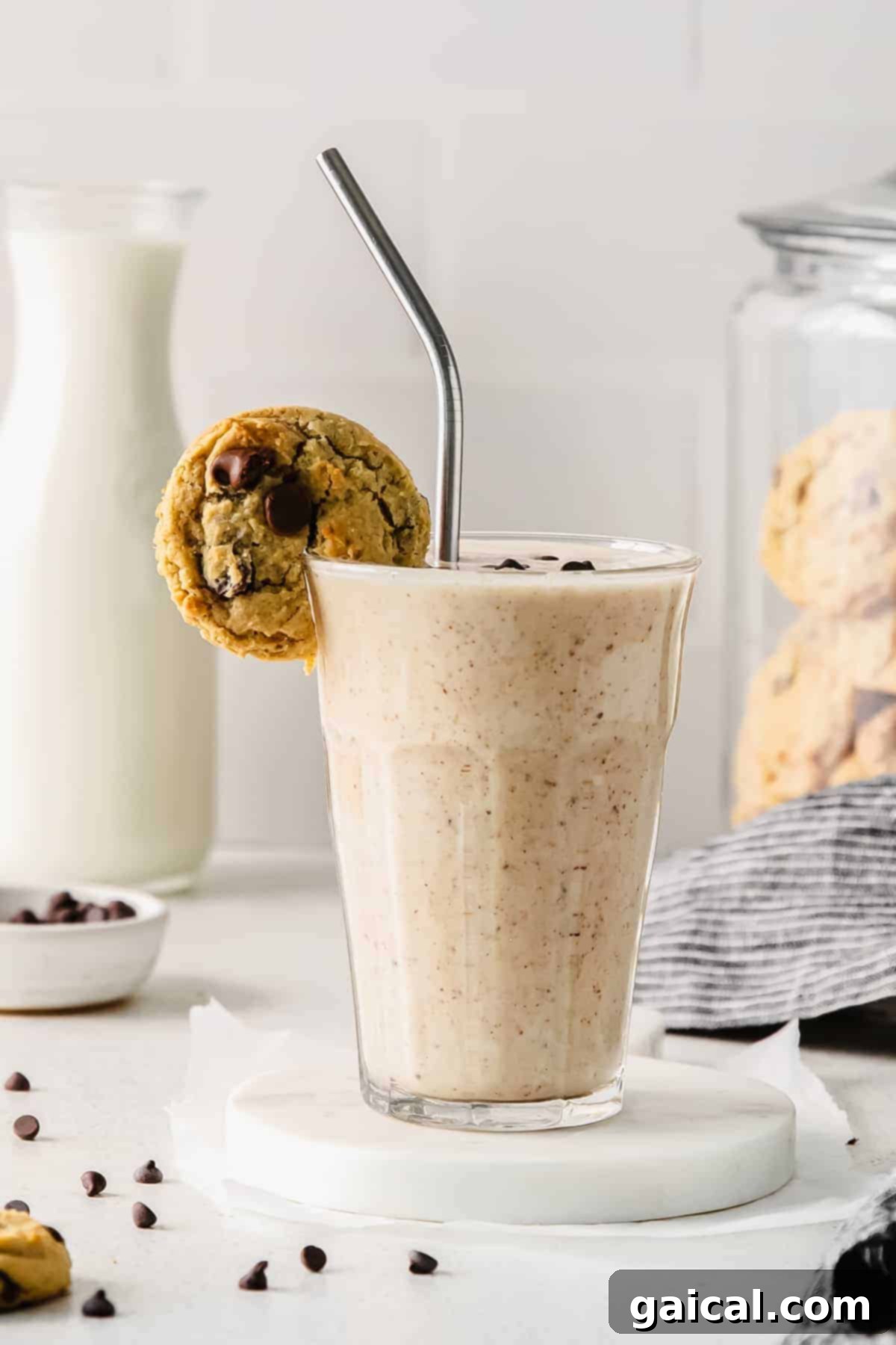 A tall glass of creamy cookie dough smoothie, beautifully garnished with a chocolate chip cookie resting on the rim, ready to be enjoyed.