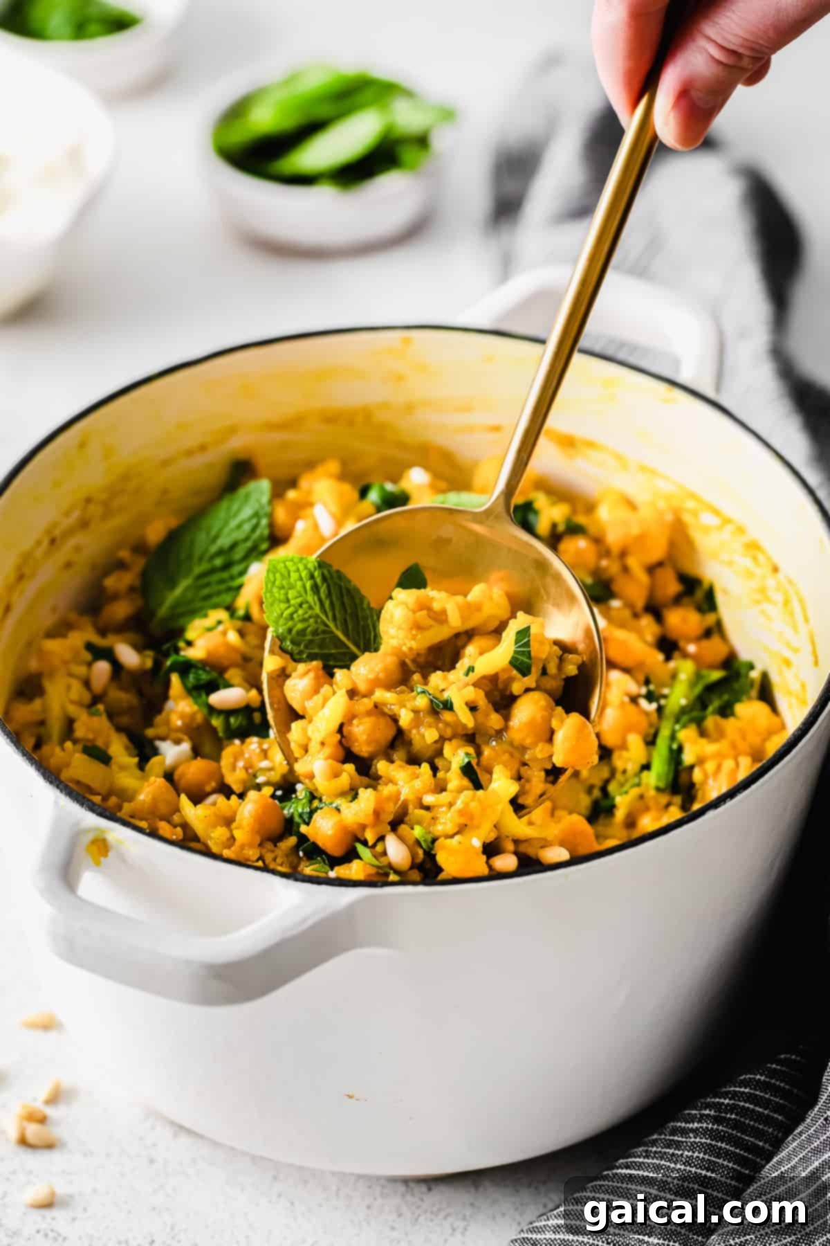 Tek Tencere Marine Nohutlu Sarı Pilav 8 A spoon lifting a portion of yellow rice with chickpeas and spinach, showing its creamy texture.