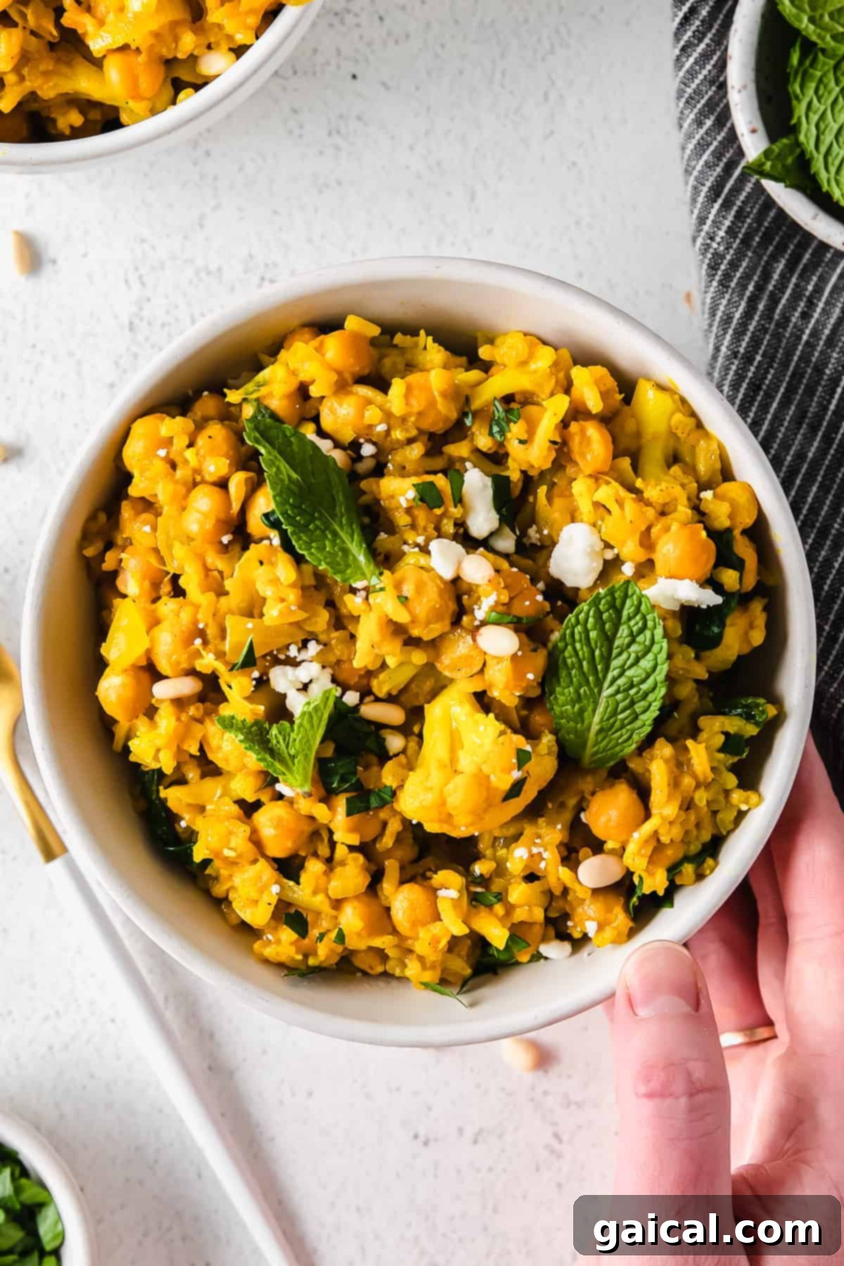 Tek Tencere Marine Nohutlu Sarı Pilav 9 A bowl of one pot yellow rice with marinated chickpeas, topped with feta crumbles and fresh herbs.