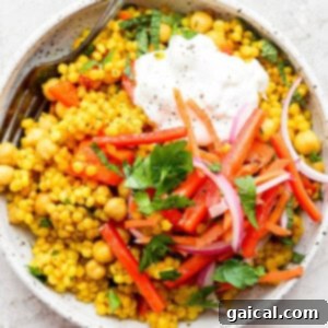 A top-down view of the finished Lemon Garlic Israeli Couscous, garnished with fresh herbs, whipped feta, and pickled vegetables, ready to be served.