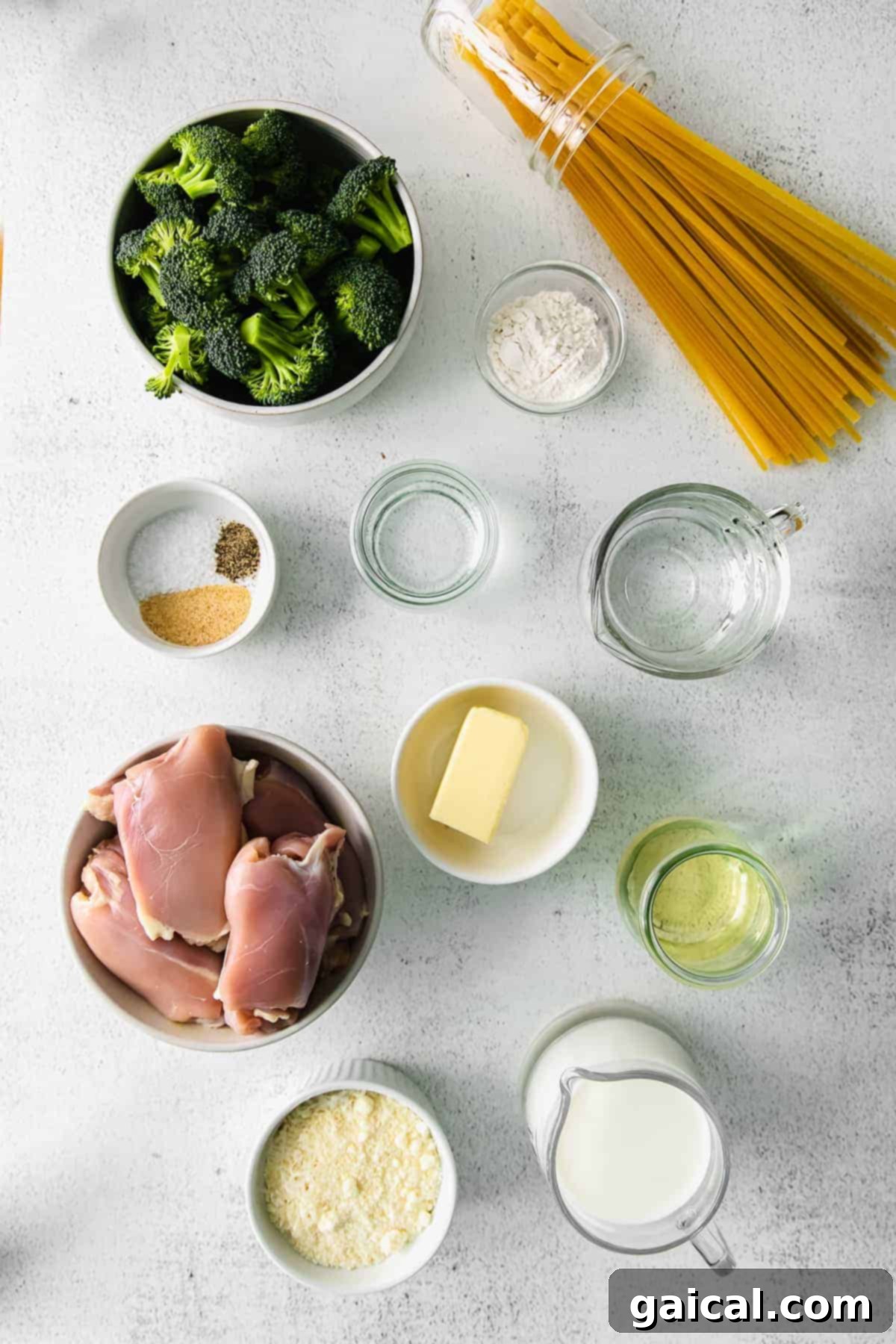 Bowls of fresh ingredients for chicken broccoli alfredo including chicken thighs, parmesan cheese, butter, milk, garlic, and pasta.