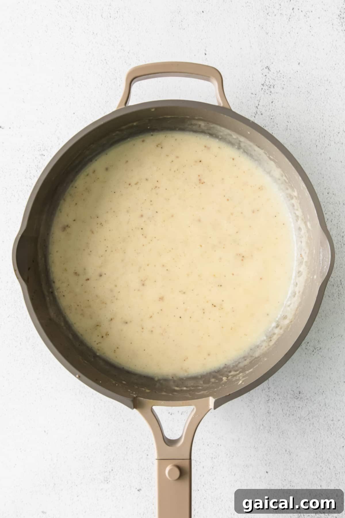 A rich and creamy alfredo sauce simmering in a pan, ready for pasta and other ingredients.