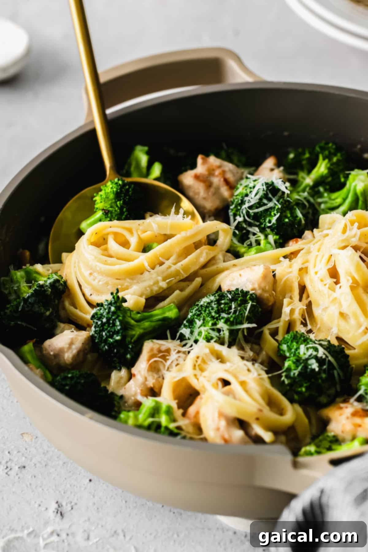A serving spoon lifting a forkful of chicken broccoli alfredo pasta with a piece of broccoli.