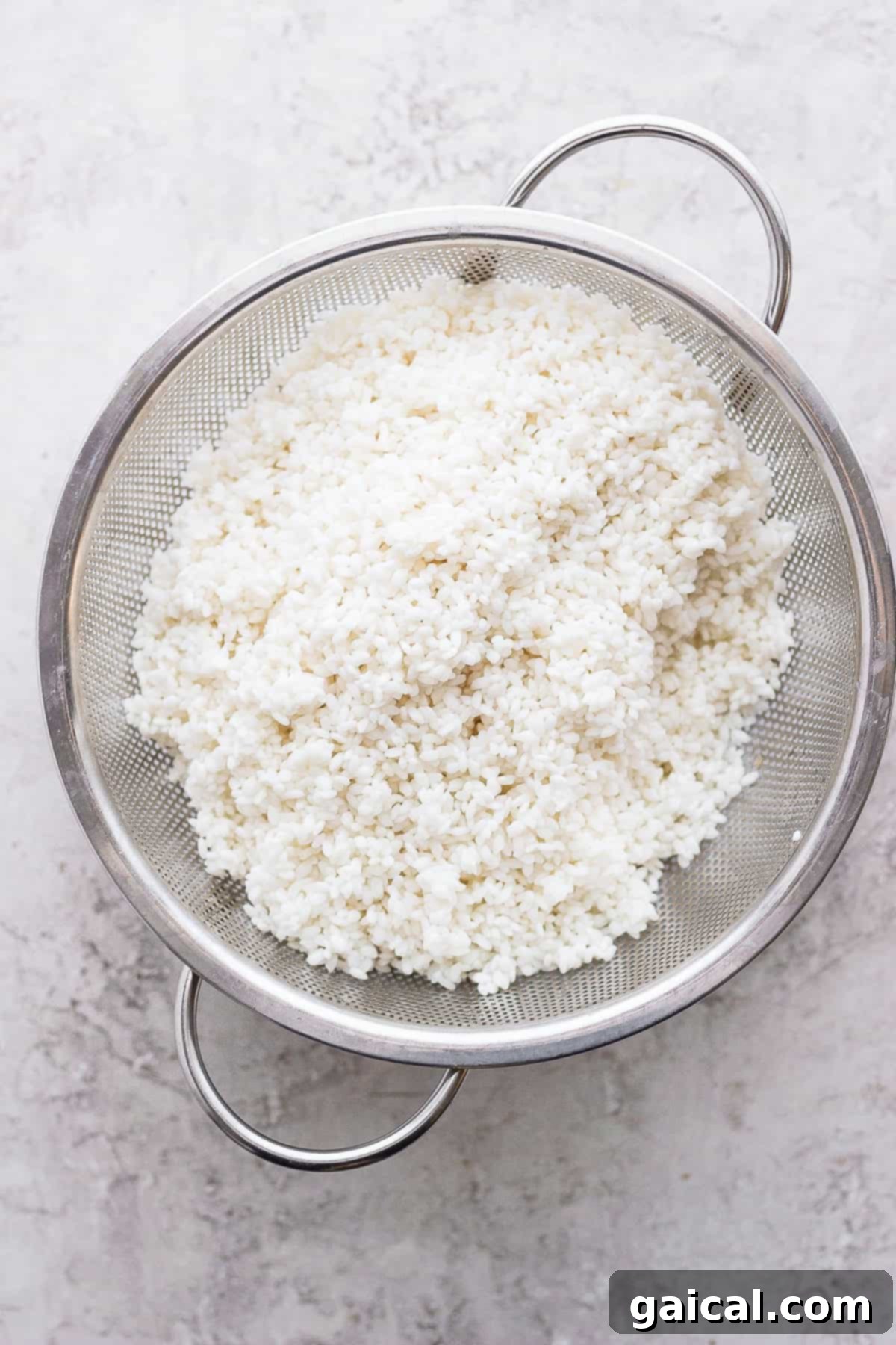 Close-up of sticky rice draining in a metal strainer after its second soak, ready for steaming.