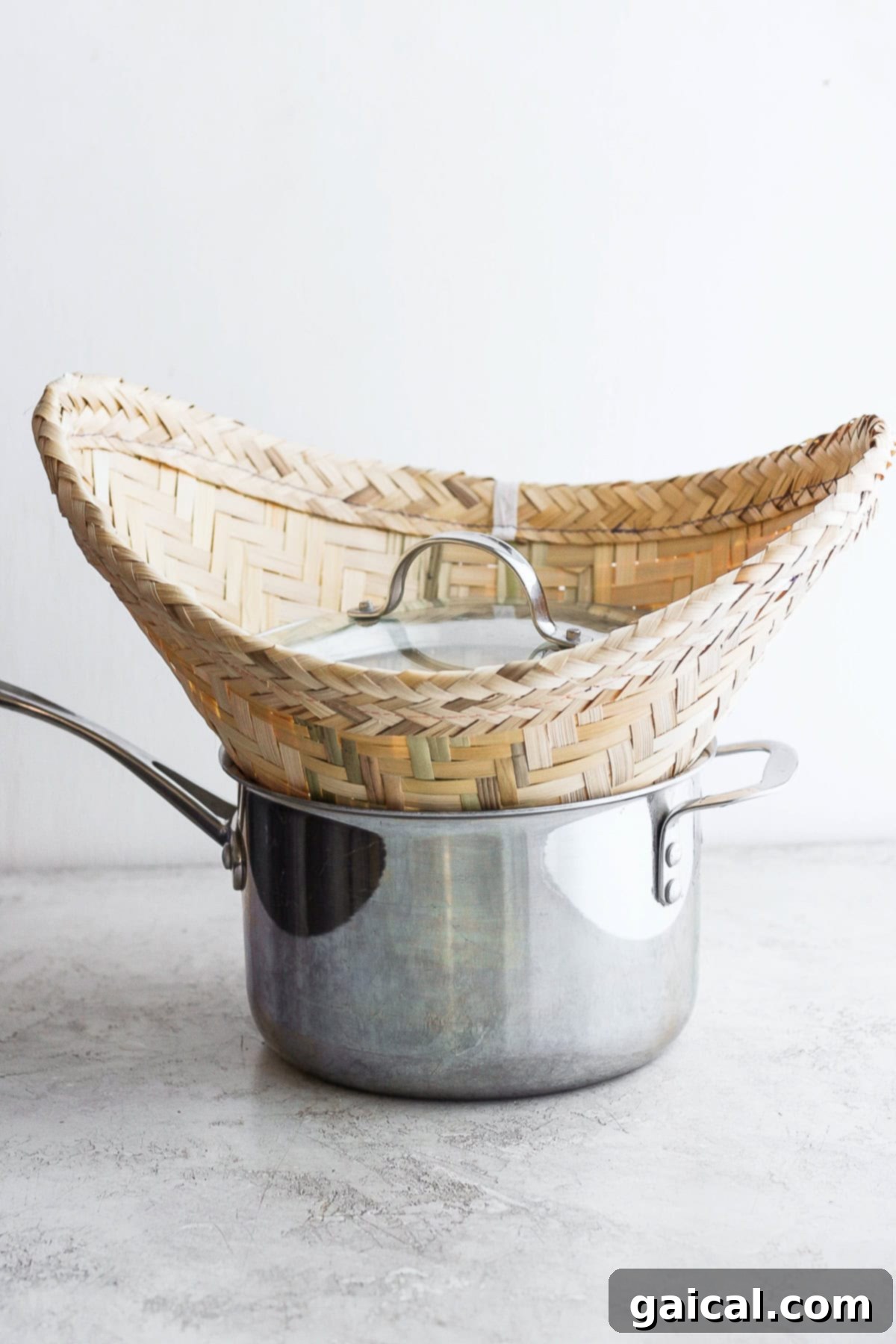 Sticky rice steaming in a bamboo basket placed over a pot of boiling water, covered with a lid.
