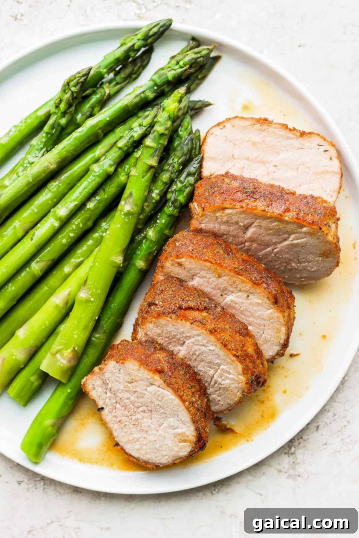 This Air Fryer Pork Tenderloin recipe is super moist on the inside with a crispy outside and is ready to enjoy in minutes. Air fryer pork tenderloin served on a plate with fresh green asparagus, ready to eat.