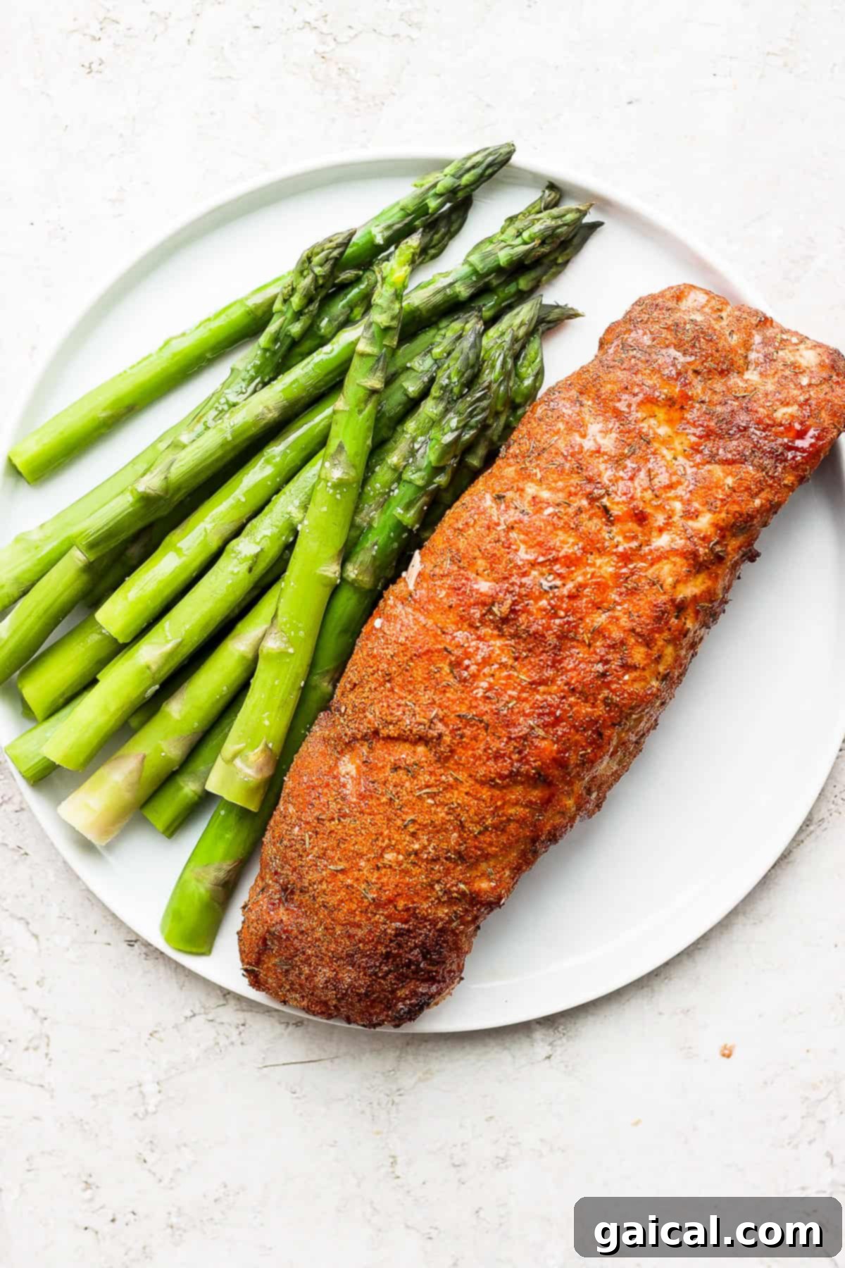 This Air Fryer Pork Tenderloin recipe is super moist on the inside with a crispy outside and is ready to enjoy in minutes. A beautifully air-fried pork tenderloin, sliced and served on a plate with fresh green asparagus, highlighting its golden crust and juicy interior.