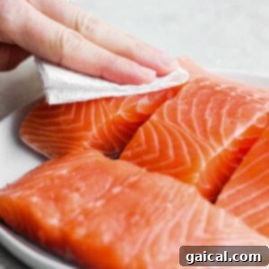 A close-up of raw salmon being blotted dry with a paper towel, a technique essential for crispy skin when air frying.