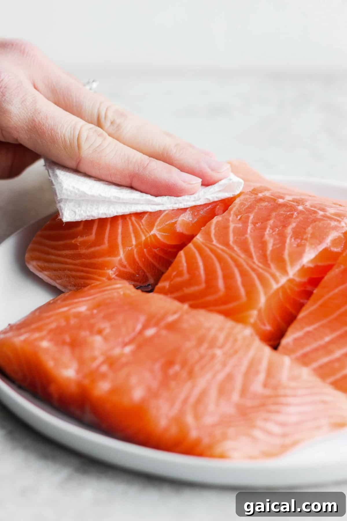 Close-up of raw salmon being patted dry with a paper towel, a crucial step for achieving crispy air-fried skin.