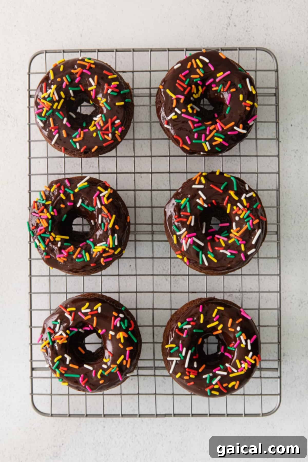 Baked Chocolate Donuts with Various Toppings Assortment of chocolate baked donuts on a wire rack, some with sprinkles