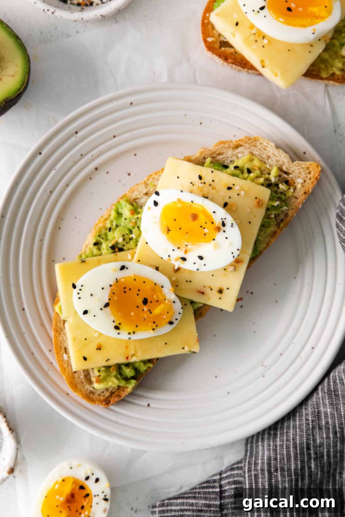 Soft-boiled egg halves placed atop a slice of avocado toast, sprinkled with seasoning