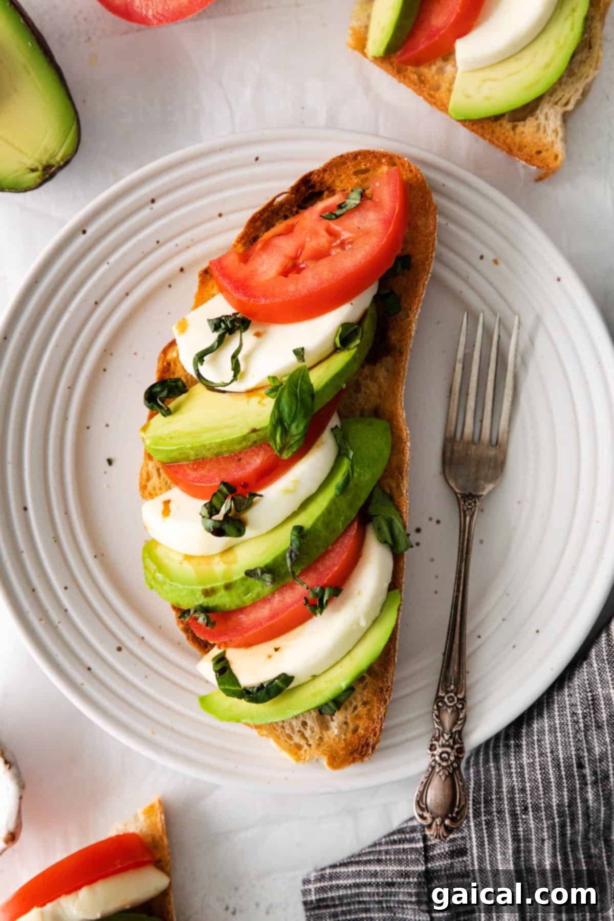 Caprese ingredients elegantly arranged on a slice of avocado toast on a white plate