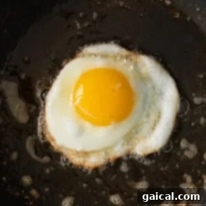 An egg being fried in a non-stick pan, with the whites setting and the yolk visible.