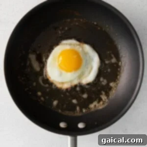 A fried egg cooking in a non-stick pan on a white background, showing the setting whites and warm yolk.