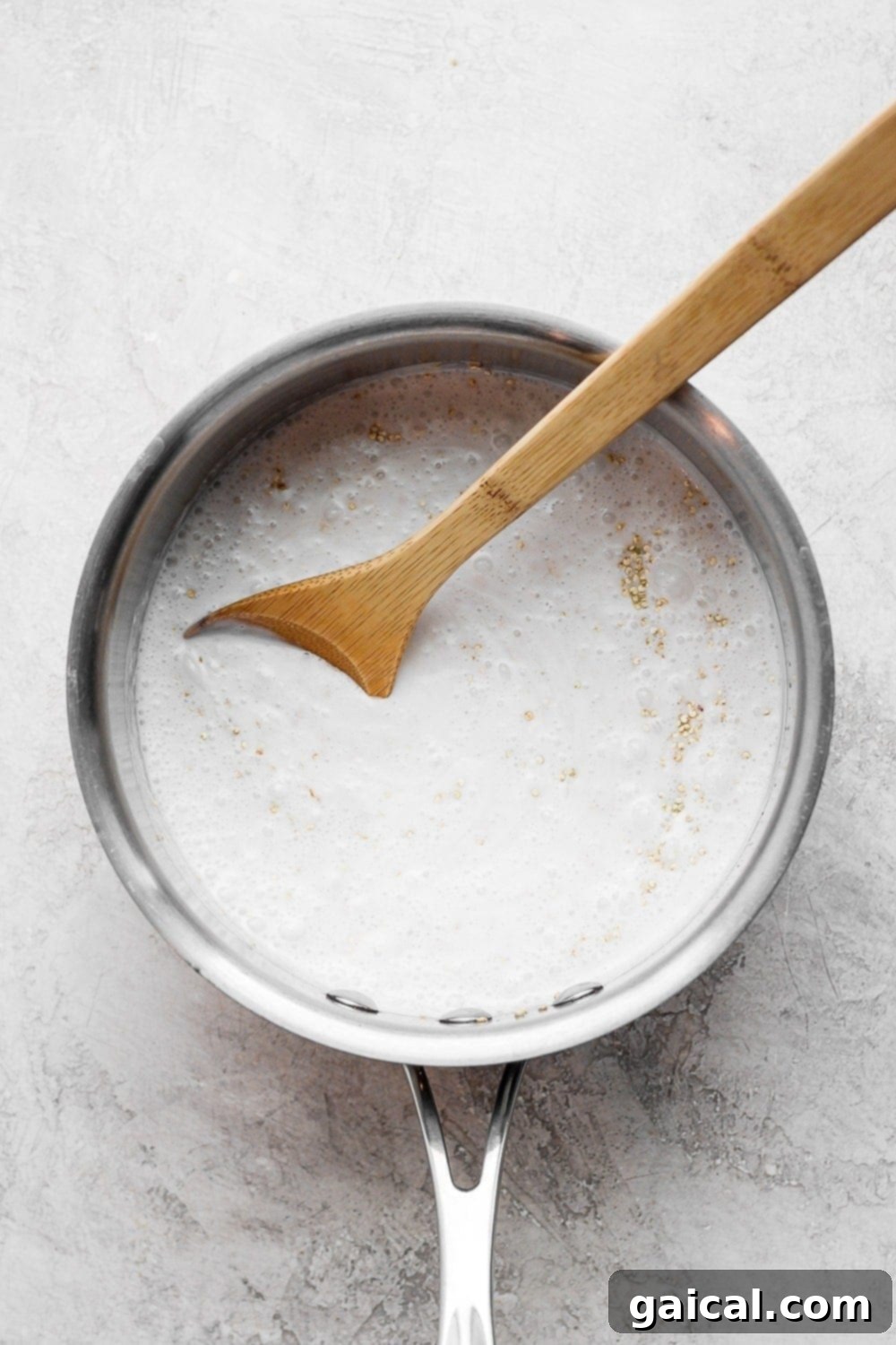 Tropical Coconut Quinoa 4 A wooden spoon gently stirring the cooking mixture of coconut milk and quinoa in a saucepan, ensuring even distribution and proper cooking.