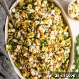 Close-up of vibrant lemon pasta salad in a white bowl, garnished with fresh herbs
