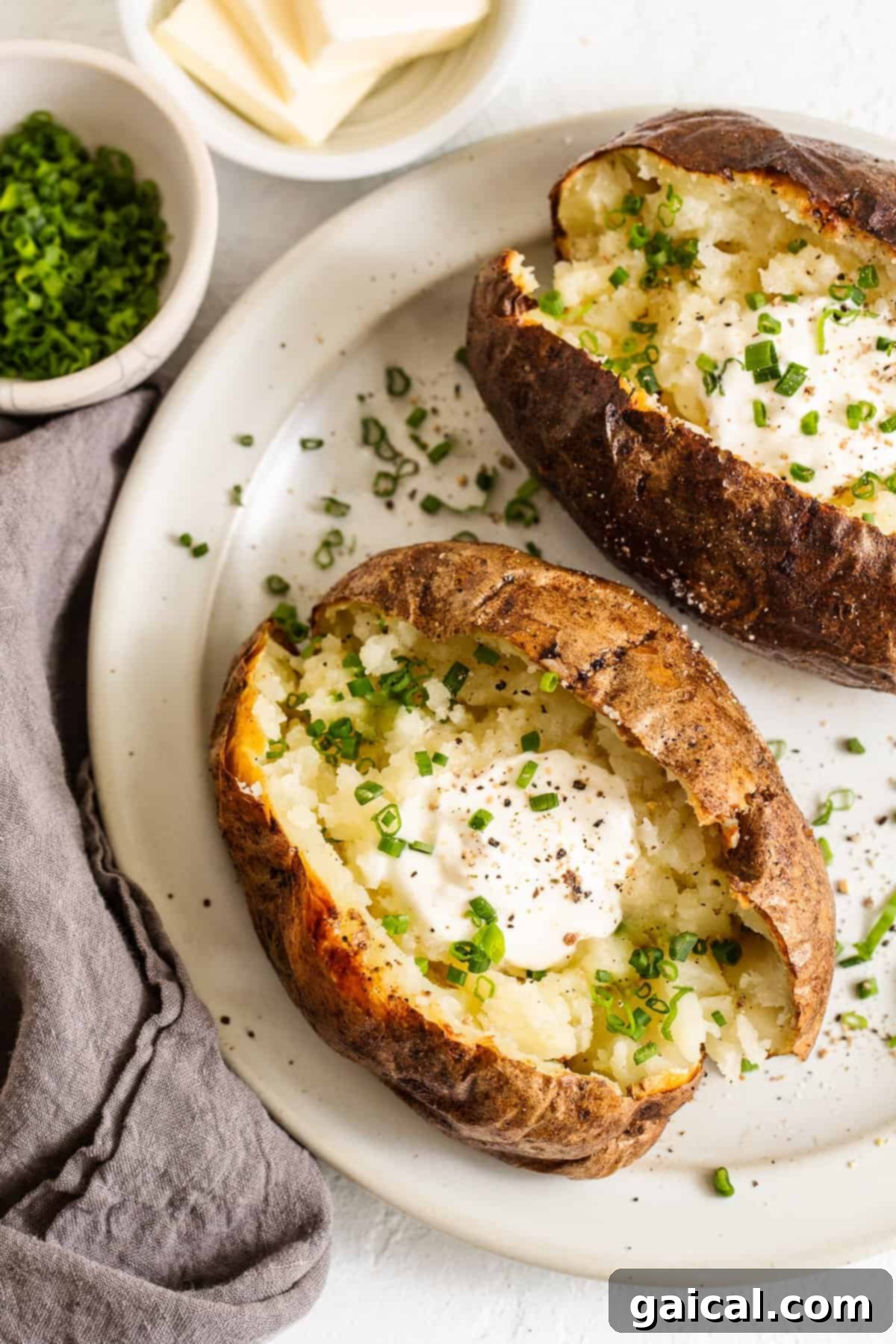Two perfectly baked russet potatoes emerging from an air fryer, steam gently rising, showcasing their golden-brown, crispy skin.