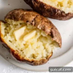 Two golden-brown air fryer baked potatoes, split open with butter melting inside, presented on a white plate.