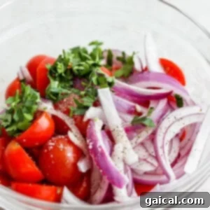 Close-up of cherry tomatoes, red onion, and parsley soaking in a bowl with a light vinaigrette.