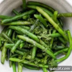 Blanched green beans with fresh mint and olive oil in a bowl, showing their vibrant green color.