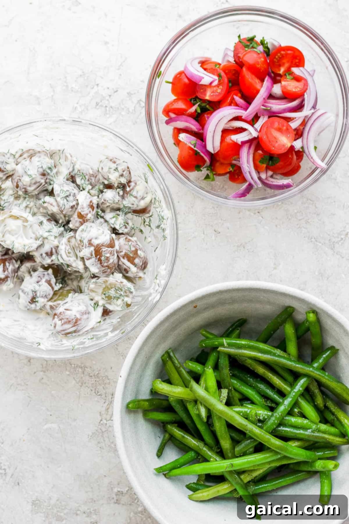 Individual ingredients for a Nicoise Salad, including tomatoes, potatoes, green beans, and canned tuna, presented in separate bowls.