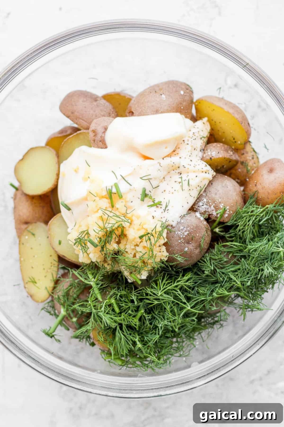 Close-up of boiled potatoes, mayonnaise, minced garlic, and fresh dill in a bowl, ready for mixing to create the creamy potato dressing.