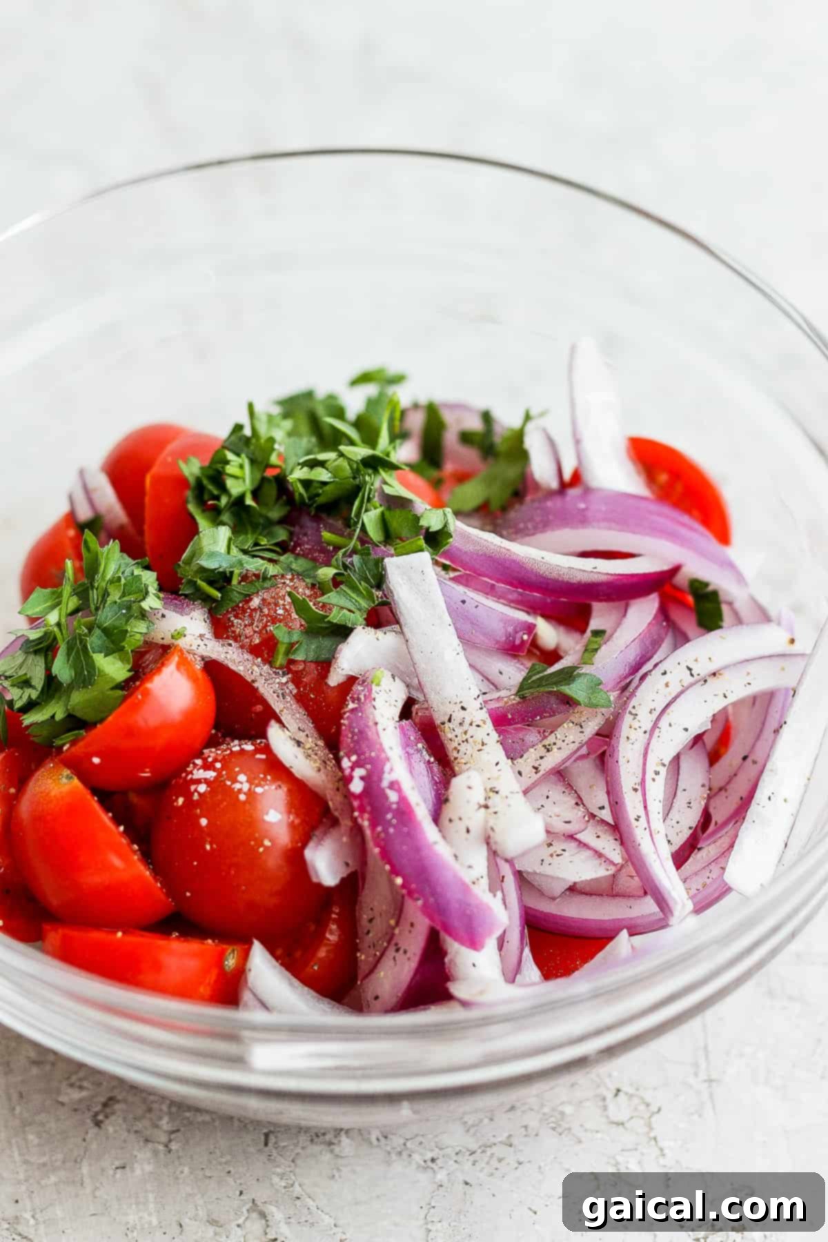 Halved cherry tomatoes, thinly sliced red onion, and fresh parsley mixed in a bowl with a light vinaigrette.