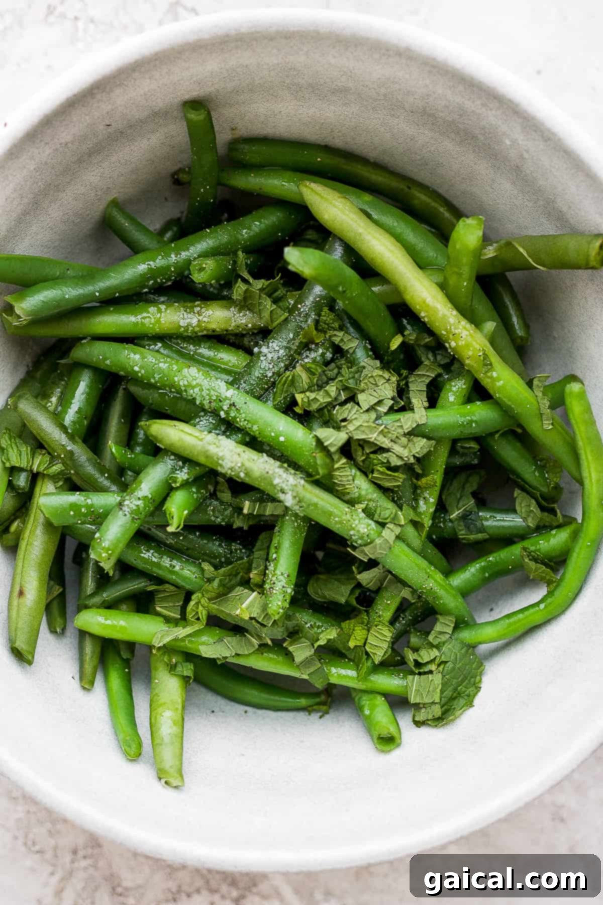 Vibrant blanched green beans tossed with fresh mint leaves in a bowl, highlighting their crisp texture and appealing color.