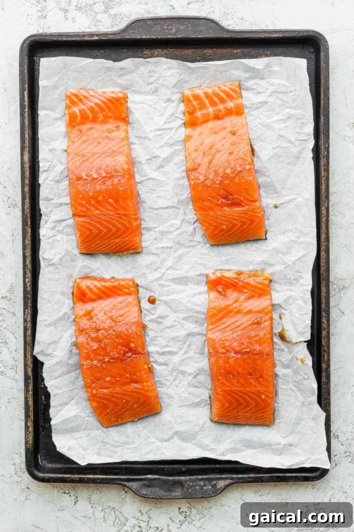 Salmon Fillets Ready for Broiling Four salmon fillets evenly spaced on a parchment-lined baking sheet, ready for broiling, showing preparation stage.
