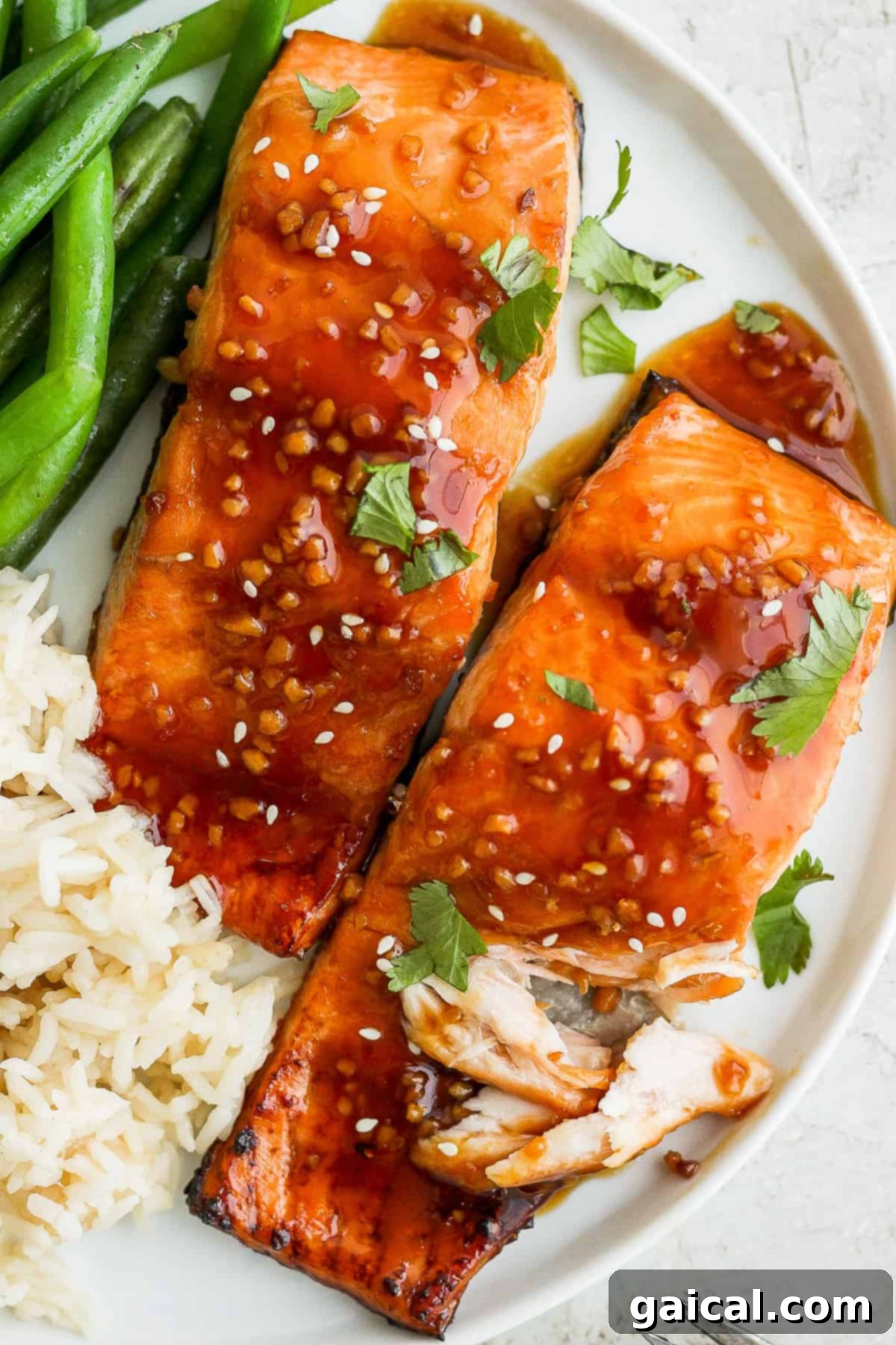 Finished Teriyaki Salmon Dish Beautifully plated teriyaki salmon, garnished with sesame seeds and green onions, served with rice and green beans, ready to eat.