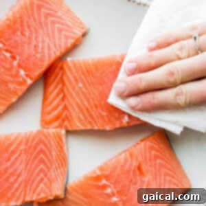 Sticky Teriyaki Salmon 5 A person is holding a piece of salmon on a plate, demonstrating the first step of patting dry.