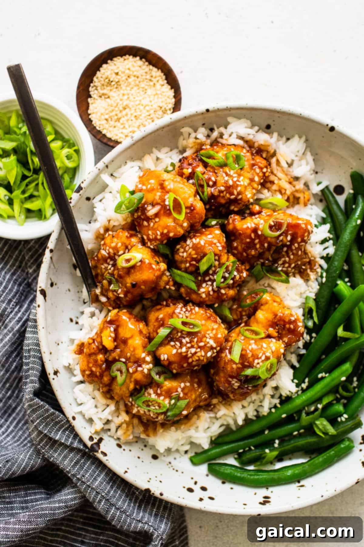This saucy, delicious air fryer honey sesame chicken is ready in 30 minutes and tastes deep-fried, but it's actually made in the air fryer! sesame chicken in bowl with veggies