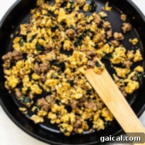 Scrambled eggs in a skillet with a wooden spatula.