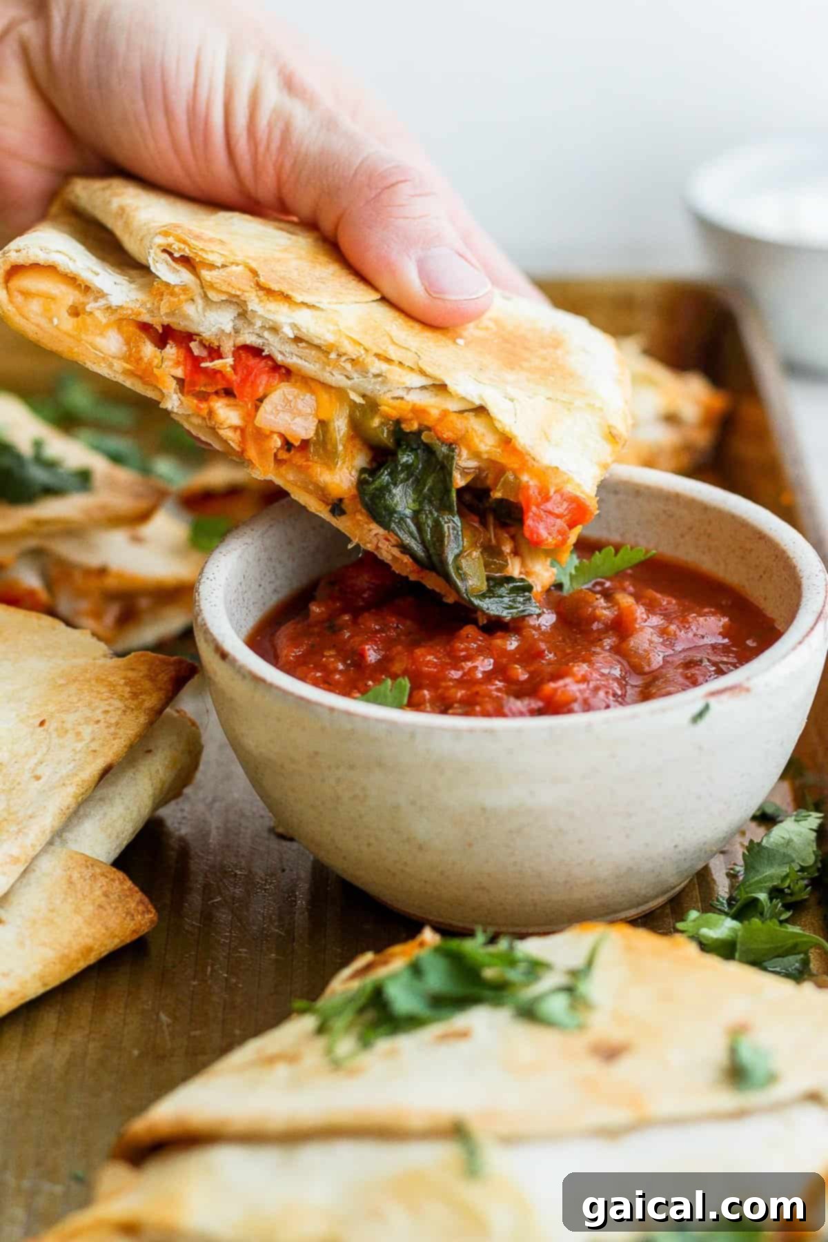 Sheet Pan Quesadilla Party 8 A hand dipping a slice of sheet pan quesadilla into a bowl of fresh salsa.