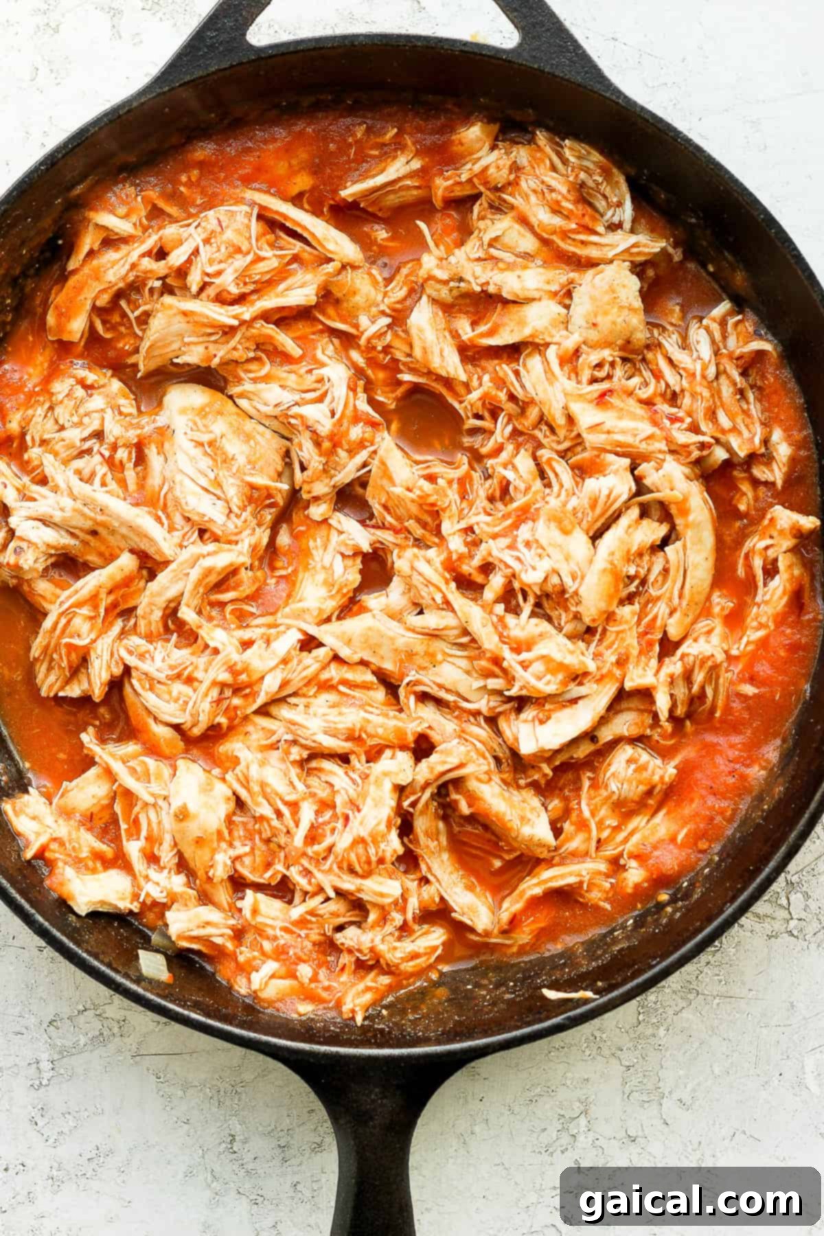 Chicken Tinga simmering in a skillet. Shredded chicken and tinga sauce in a cast iron skllet.