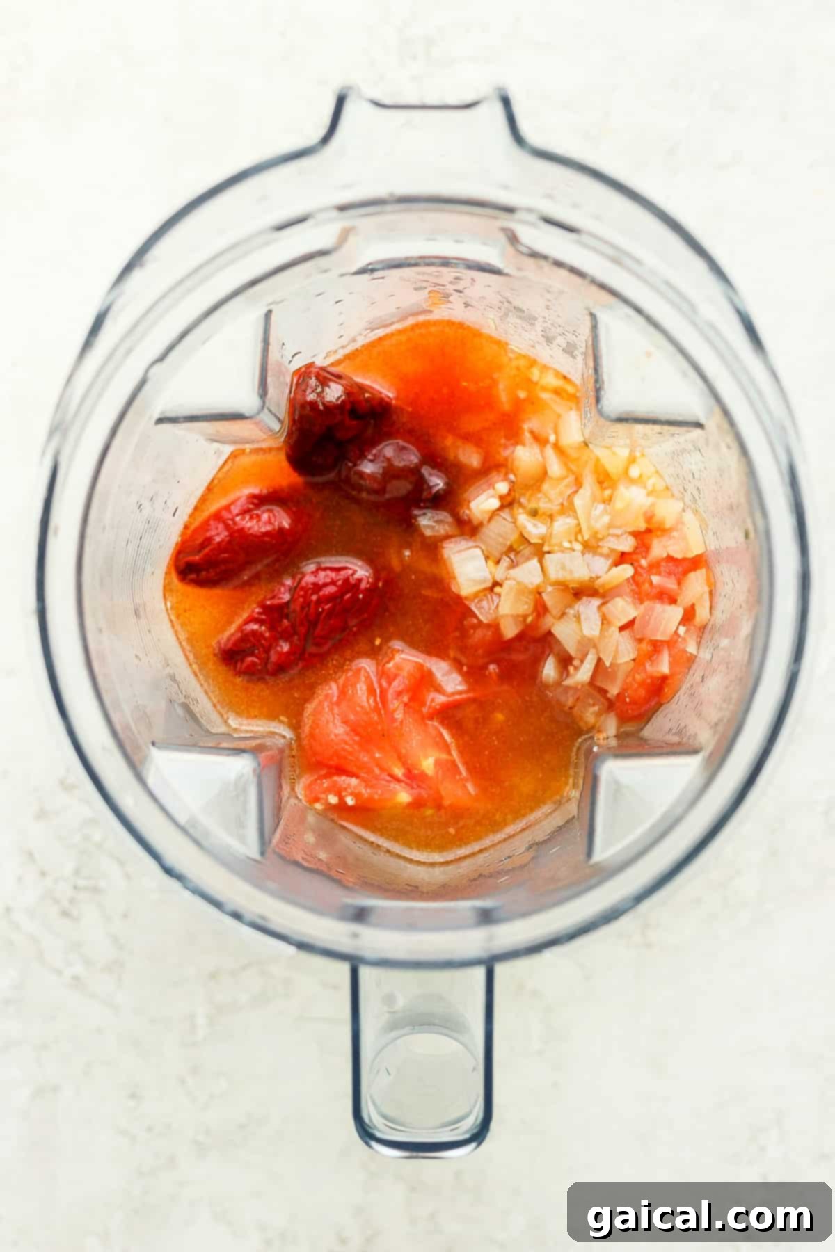 Blended sauce ingredients: tomatoes, onions, chipotles. Chicken tinga ingredients in a blender.