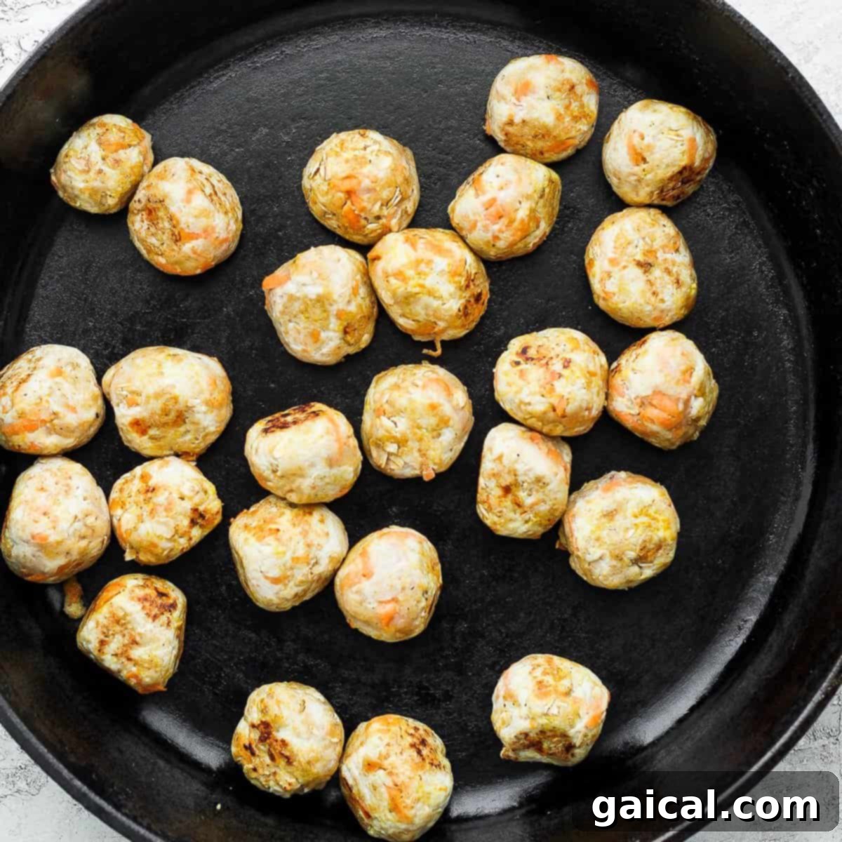Chicken meatballs browning in a cast iron pan.