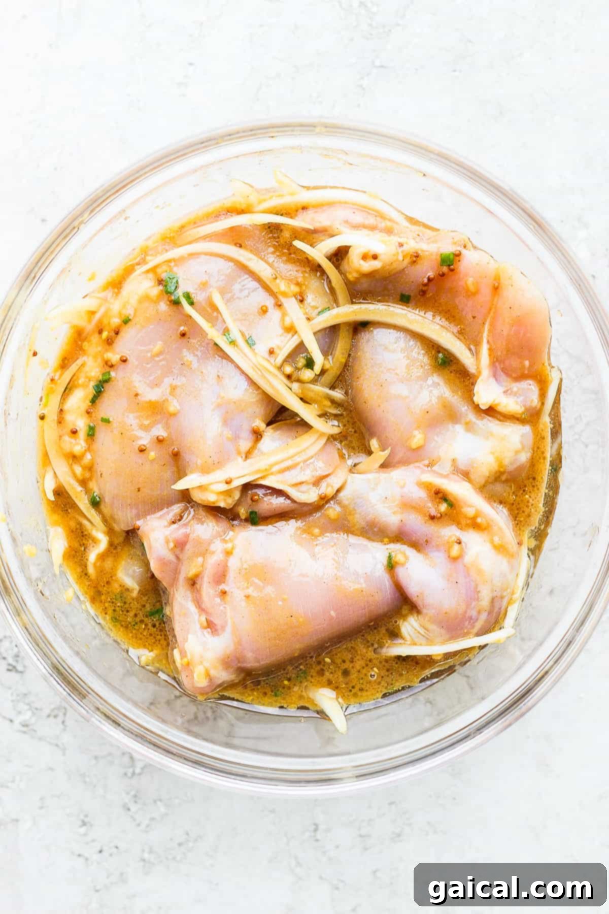 Chicken thighs marinating in a bowl with a rich honey mustard sauce.