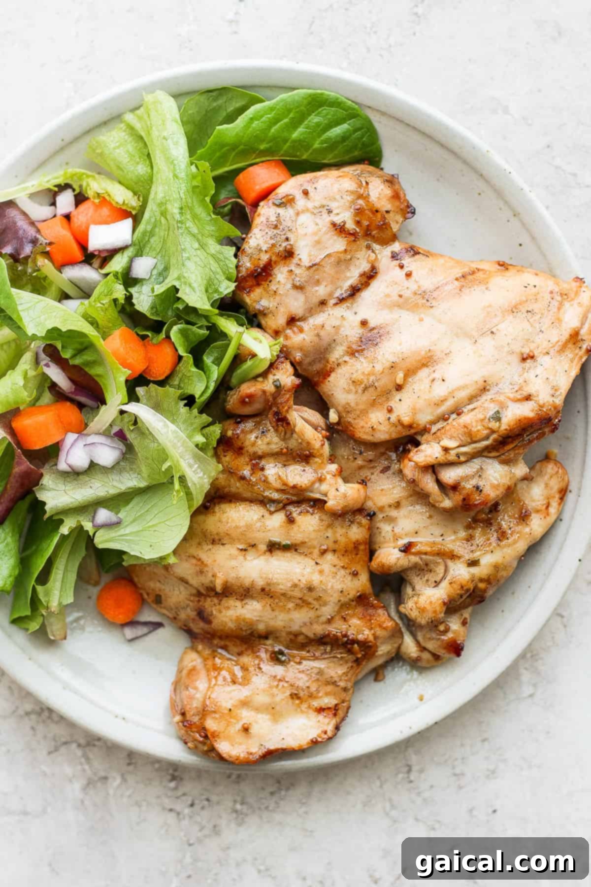Cooked honey mustard chicken thighs on a plate with a fresh salad.