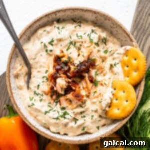 A vibrant bowl of smoked salmon dip, beautifully garnished with fresh dill, served alongside an assortment of crispy crackers and fresh vegetable sticks, creating an inviting appetizer spread.