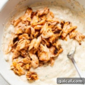 A close-up of the dip in a white bowl, now containing generous flakes of pink smoked salmon, being gently mixed with a spoon to combine.