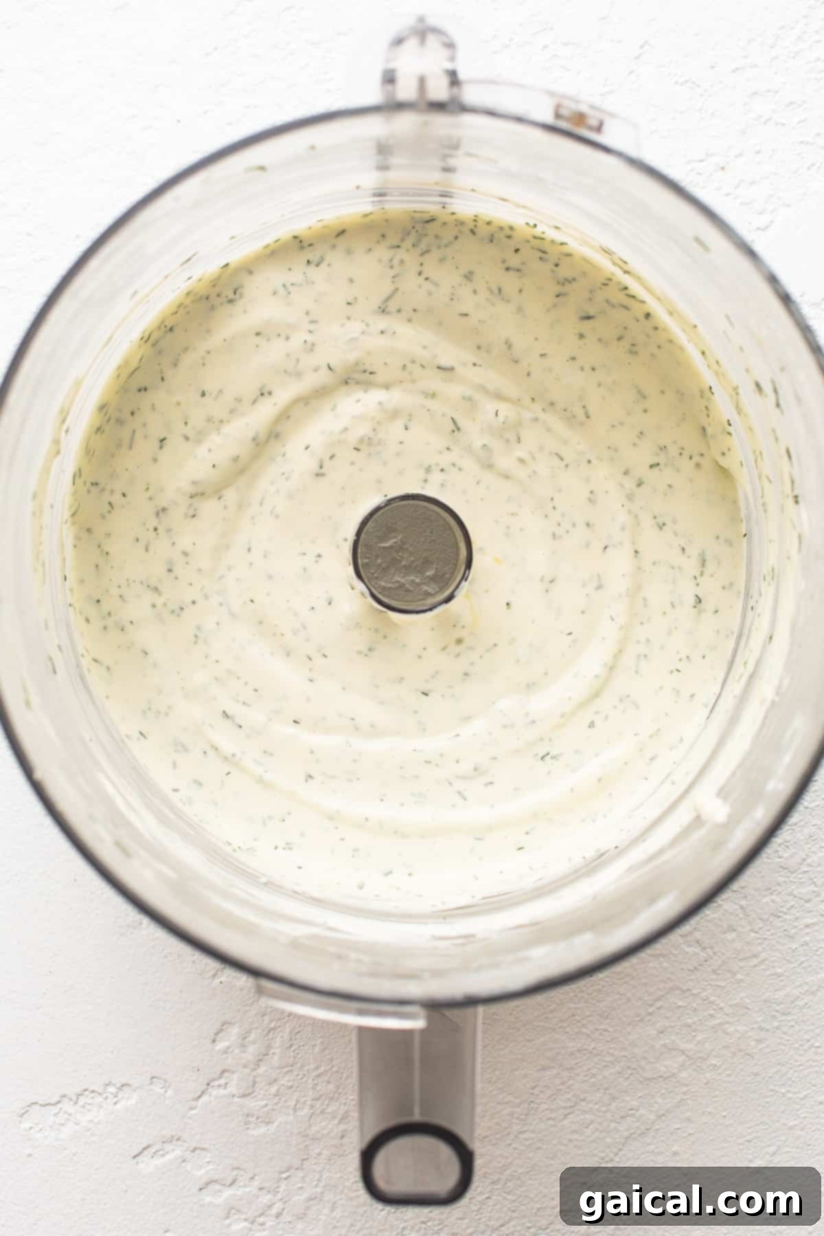 Achieving the Perfect Creamy Base in a Food Processor A close-up view of a food processor bowl containing a smooth, creamy, off-white mixture, highlighting the initial blending of the dairy ingredients for the dip.