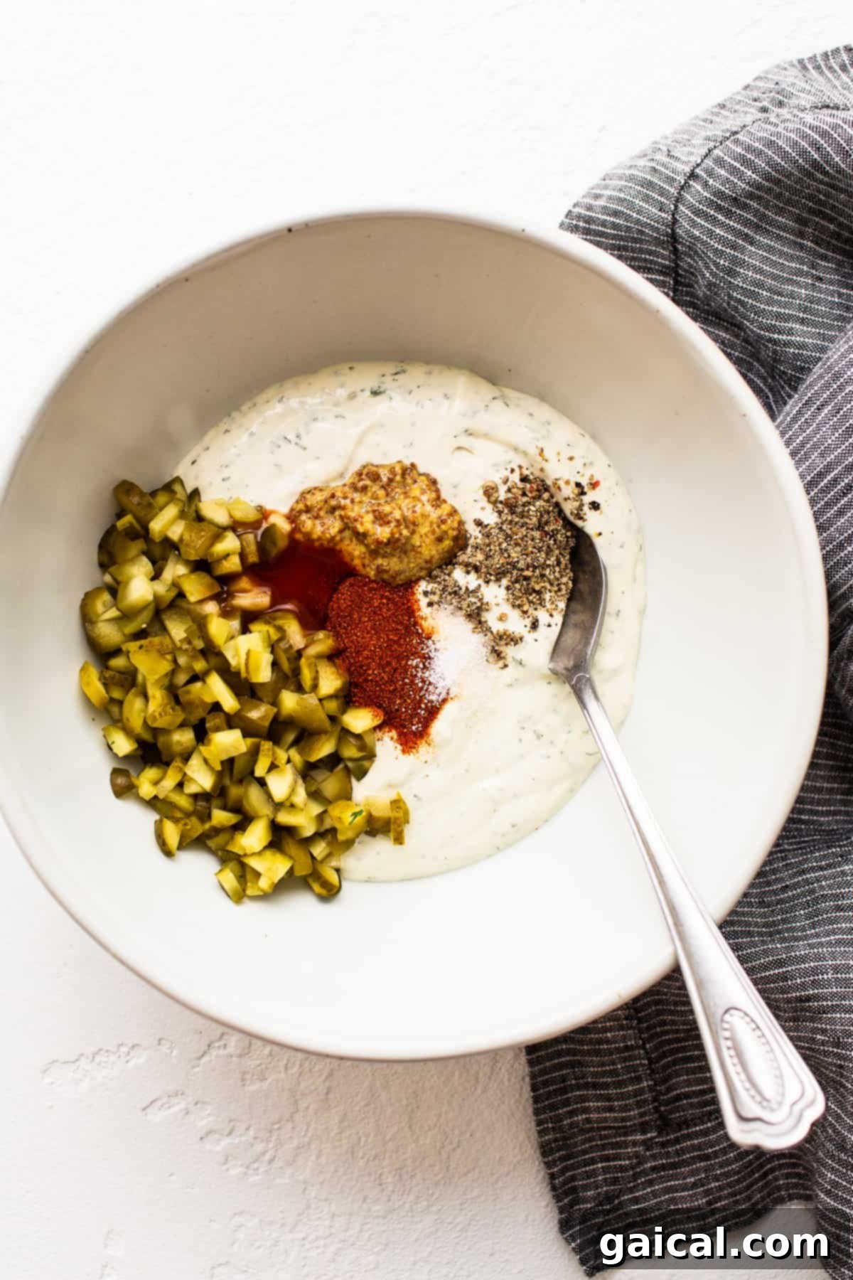 Flavorful Ingredients Blending into the Creamy Dip Base A vibrant bowl of creamy white dip with visible green specks of dill and chopped pickles, illustrating the mix of ingredients before the salmon is added, signifying the perfect texture and flavor base.