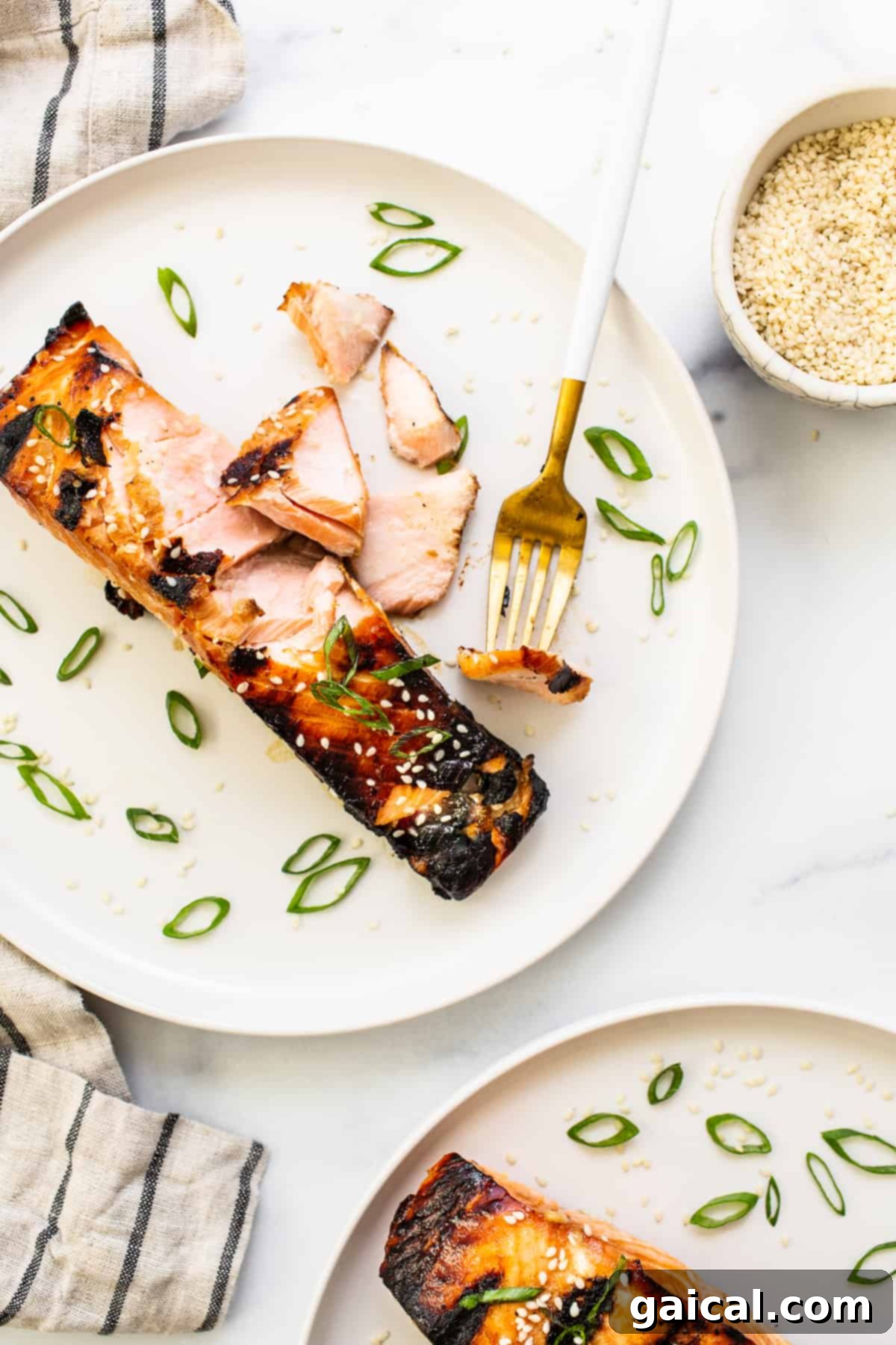 This yummy honey glazed salmon comes our caramelized and flakey. It's made with honey, soy sauce, and fresh ginger! A close-up of a perfectly flakey honey glazed salmon fillet being gently separated with a fork on a white plate.
