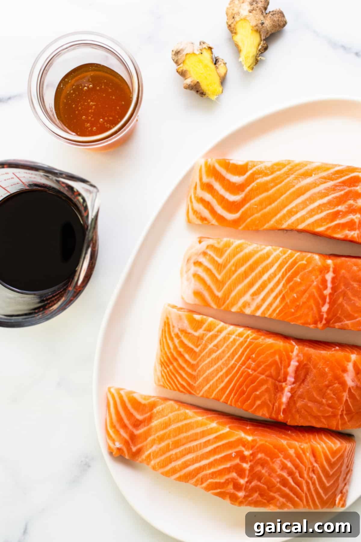 This yummy honey glazed salmon comes our caramelized and flakey. It's made with honey, soy sauce, and fresh ginger! Four raw salmon fillets arranged neatly on a platter, ready for marinating and cooking.